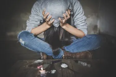 Foto van verslaafde met handen op het hoofd en verschillende soorten drugs voor zich