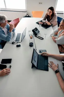 Aan een vergadertafel zitten artsen en zorgprofessionals van een instelling in overleg.