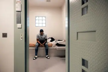 gedetineerde zit op bed in zijn cel