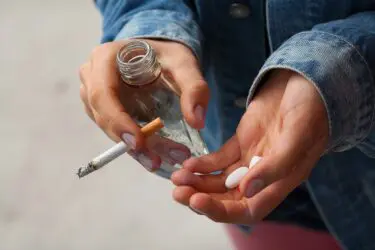 Afbeelding van handen met een fles alcohol, een sigaret en pillen