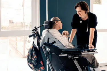 Foto van huisarts gebogen over een patient met beperking in een rolstoel.
