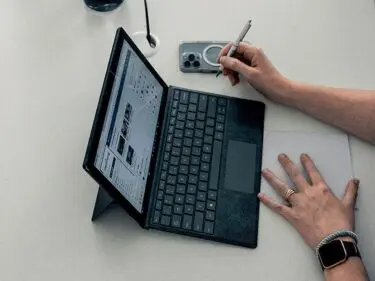 Foto van een opgeslagen laptop met daarnaast een telefoon en handen die ermee aan het werk zijn