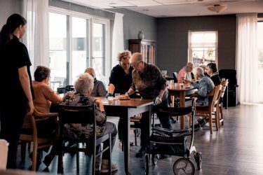 ouderen zitten in een gezamenlijke ruimte aan tafel