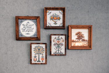 Foto met 5 lijstjes aan de wand met geborduurde spreuken en afbeeldingen.