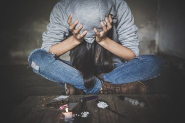 Foto van verslaafde met handen op het hoofd en verschillende soorten drugs voor zich