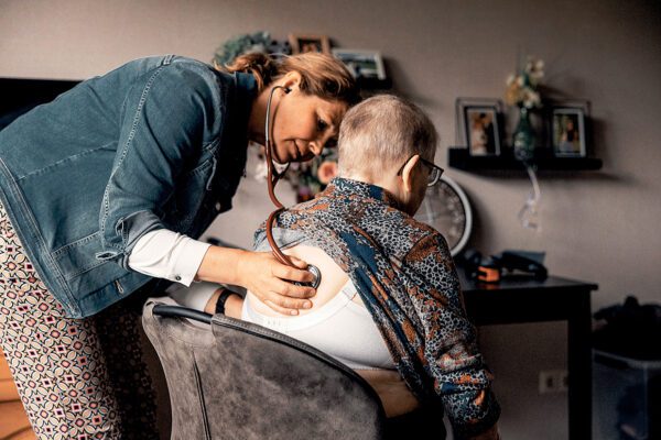 Dokter onderzoekt oude dame met stethoscoop op de rug