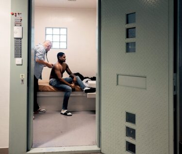 Huisarts onderzoekt gedetineerde met stethoscoop in gevangeniscel