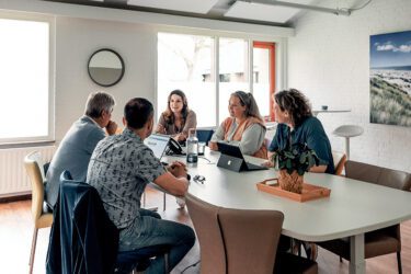 Mensen aan tafel tijdens het advies geven aan zorgorganisaties bij de implementatie en evaluatie, zodat de zorg continu verbetert en optimaal aansluit op de behoeften van de kwetsbare patiënt.