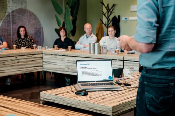 Meerdere artsen in een zaal aan tafel die onderwijs krijgen met een laptop op de voorgrond.