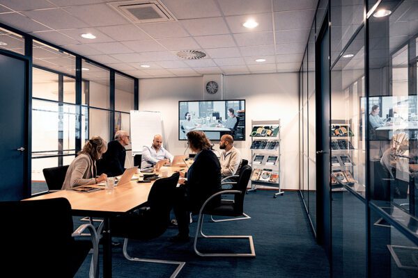 In het aquarium zitten collega's te vergaderen rond de tafel. Screen staat aan met presentatie