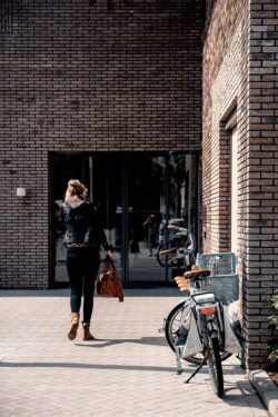 Foto van huisarts die met dokterstas naar de ingang van een verpleeghuis loopt. Op de voorgrond een fiets.