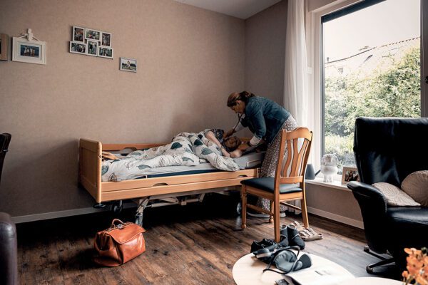 Huisarts onderzoekt een oudere patient die in bed ligt.