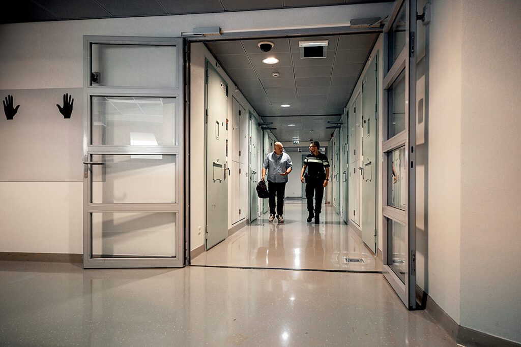 Afbeelding van justitieel geneeskundige die samen met agent door gang van arrestantencomplex loopt