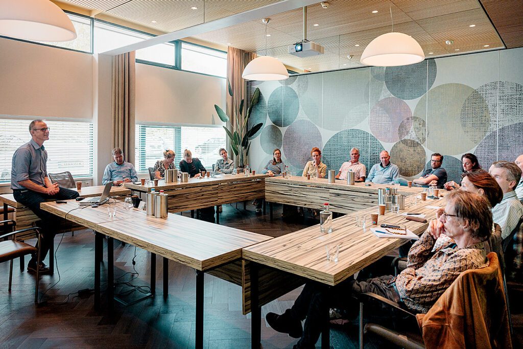 Foto van scholing met 15 mensen luisterend naar docent in een ronde setting aan tafel