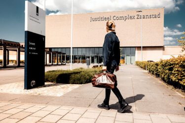 Afbeelding van huisarts die buiten het Jusititeel complex Zaanstad richting de ingang loopt.