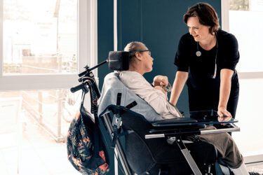Foto van huisarts gebogen over een patient met beperking in een rolstoel.