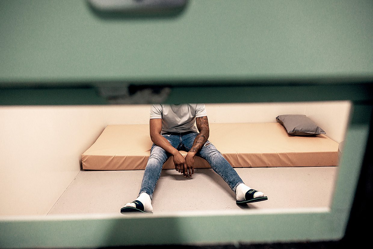 Foto van arrestant zittend in cel op matras op de grond.