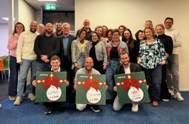 Foto van ongeveer 20 collega's die borden tonen waarop de financiele uitslag van de waardebon kerst 2025 te zien is.