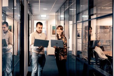 twee collega's staan naast elkaar met een laptop in hun hand