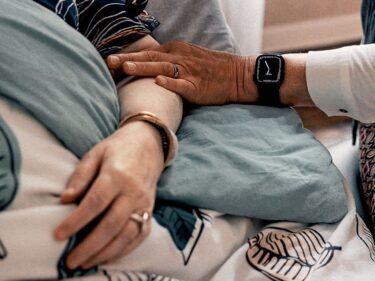 Foto van een arm die rust op een patient in bed ter geruststelling
