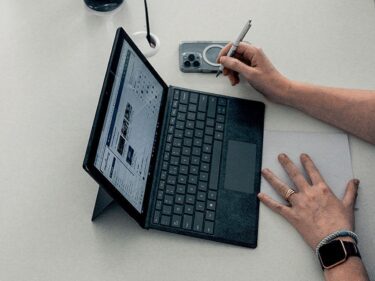 Foto van een opgeslagen laptop met daarnaast een telefoon en handen die ermee aan het werk zijn